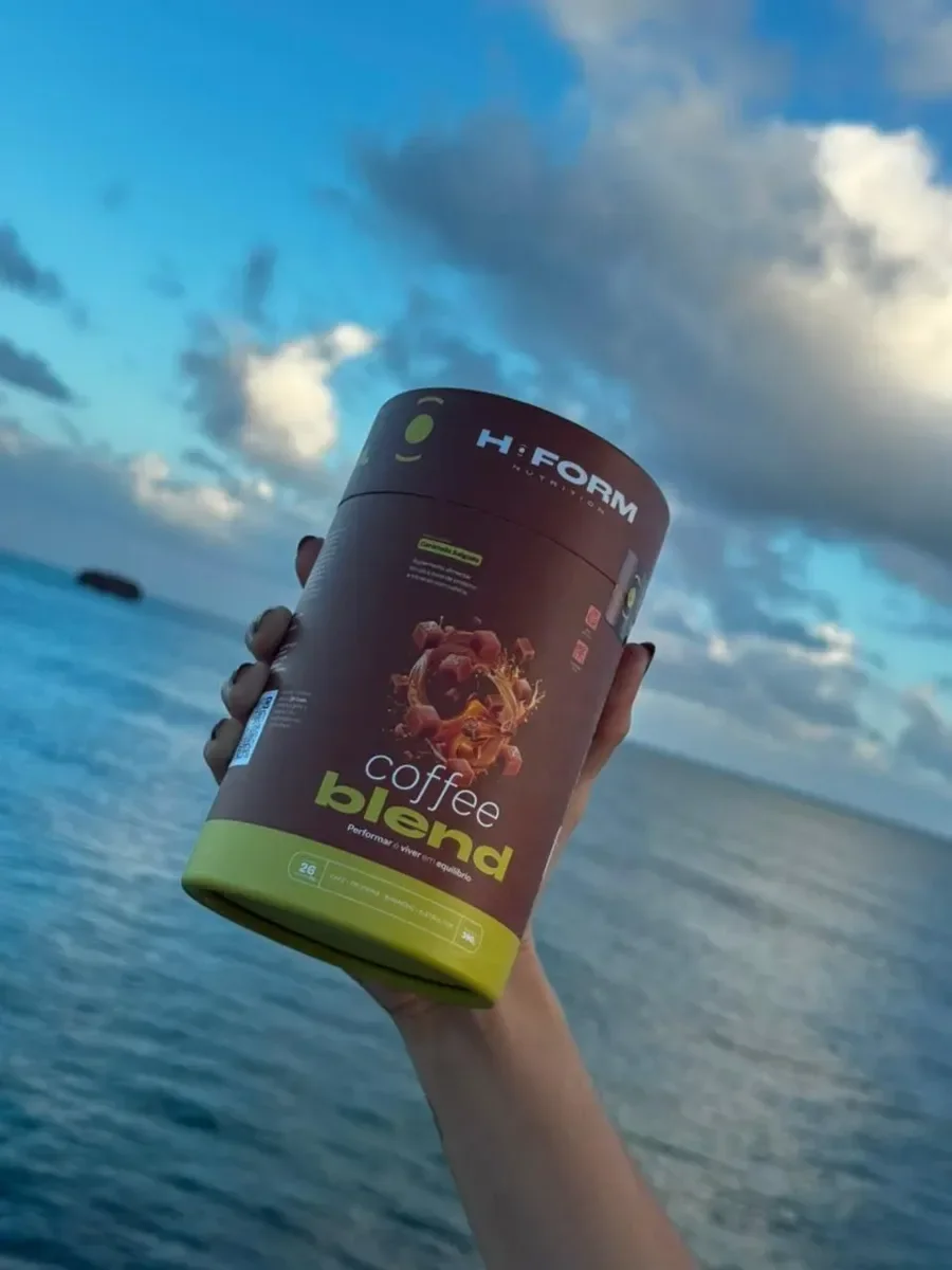 Mão erguendo o pote de Coffee Blend contra o céu e o mar